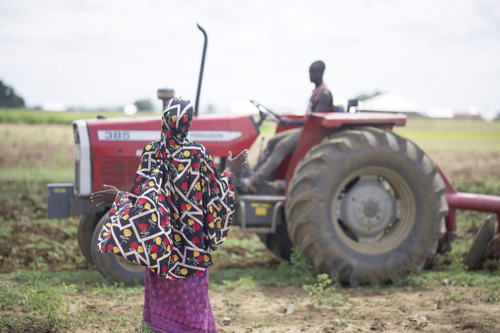 A woman interacting with a tractor operator on her farm.